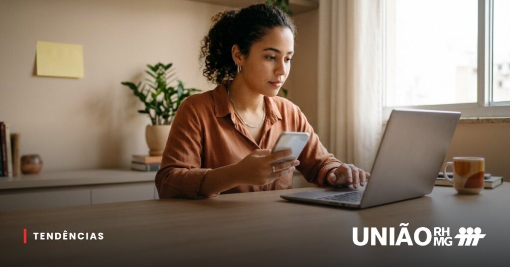 Novo colaborador enviando documentos de admissão pelo celular e pelo notebook em uma mesa de casa